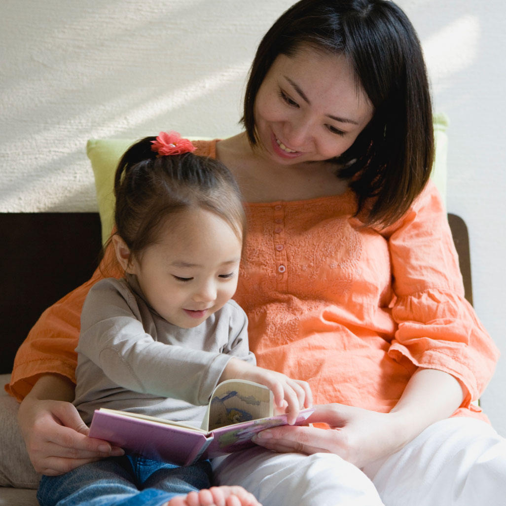 woman sitting next to small child reading a book together