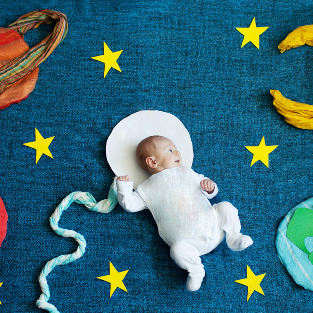 baby laying on a blanket with make shift solar system surrounding him