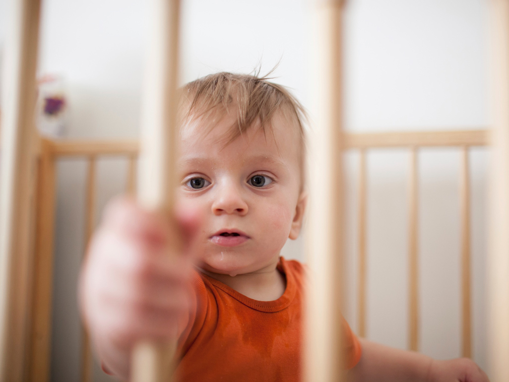 child sitting in baby crib and holding wooden slat