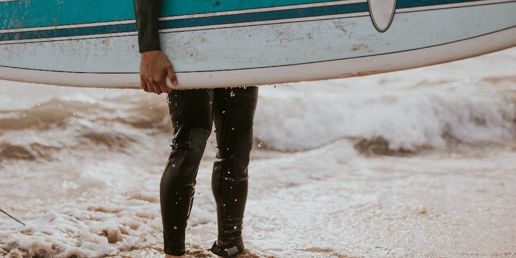 Male surfer standing with board at water's edge