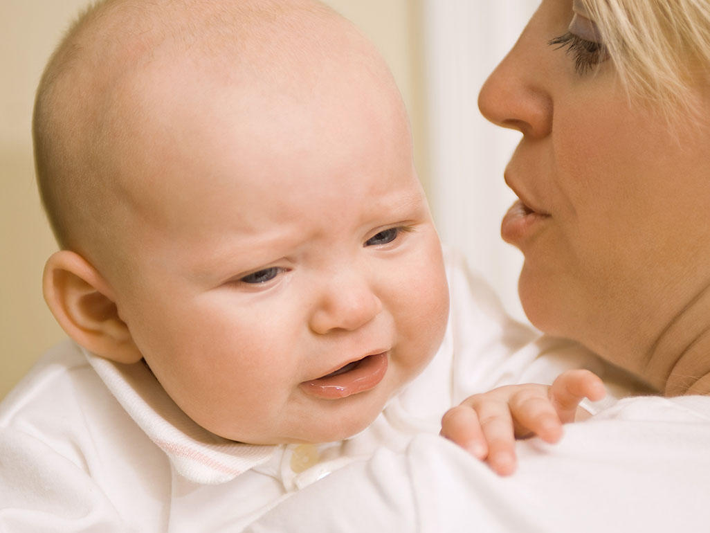 woman holding a crying baby on her shoulder