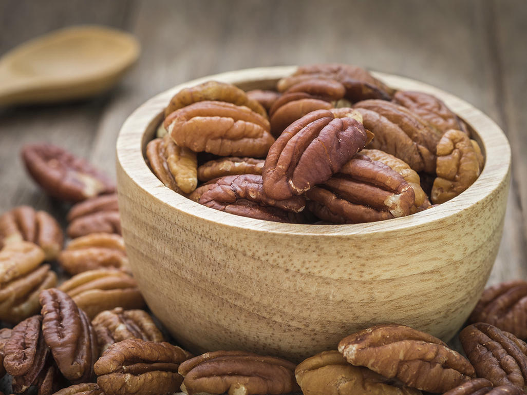 wooden bowl filled with pecans surrounded by pecans