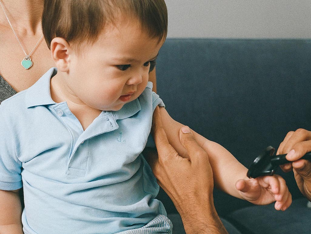 toddler sitting on adults lap while medical professional exams his arm