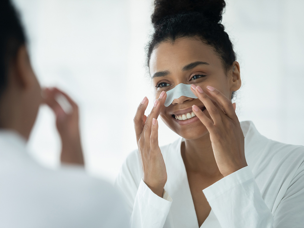 Woman looks in mirror while putting skin cleansing patch on her nose.