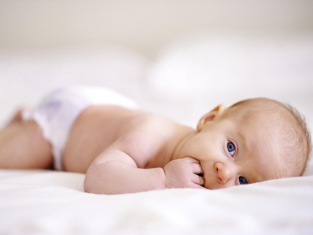 baby lying on his stomach chewing his fingers