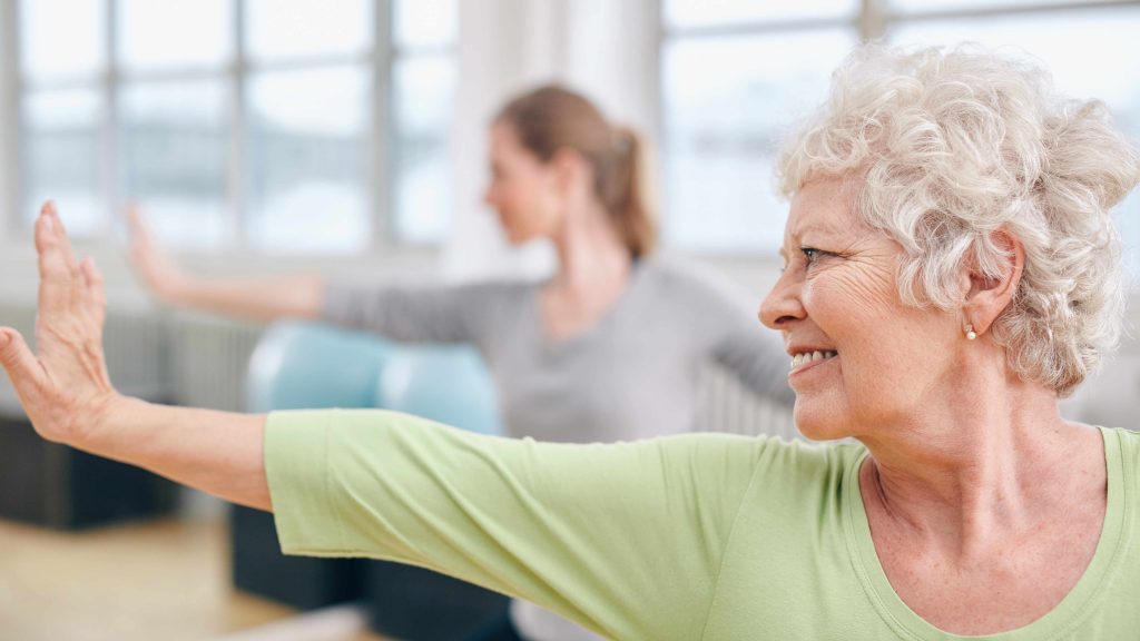 a close-up of a smiling older woman doing stretching exercises in a gym