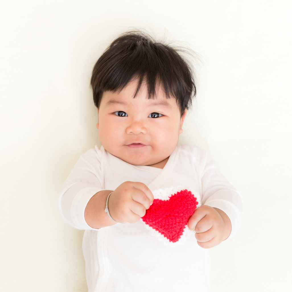 adorable baby laying down while holding a knitted heart