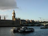 A large clock tower and other buildings line a great river.