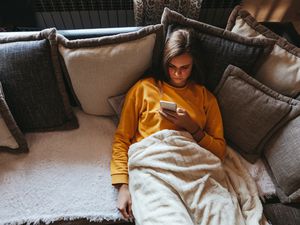 Young woman lying on sofa at living room and using cell phone at home