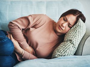 Shot of a young woman experiencing stomach pain while lying on the sofa at home