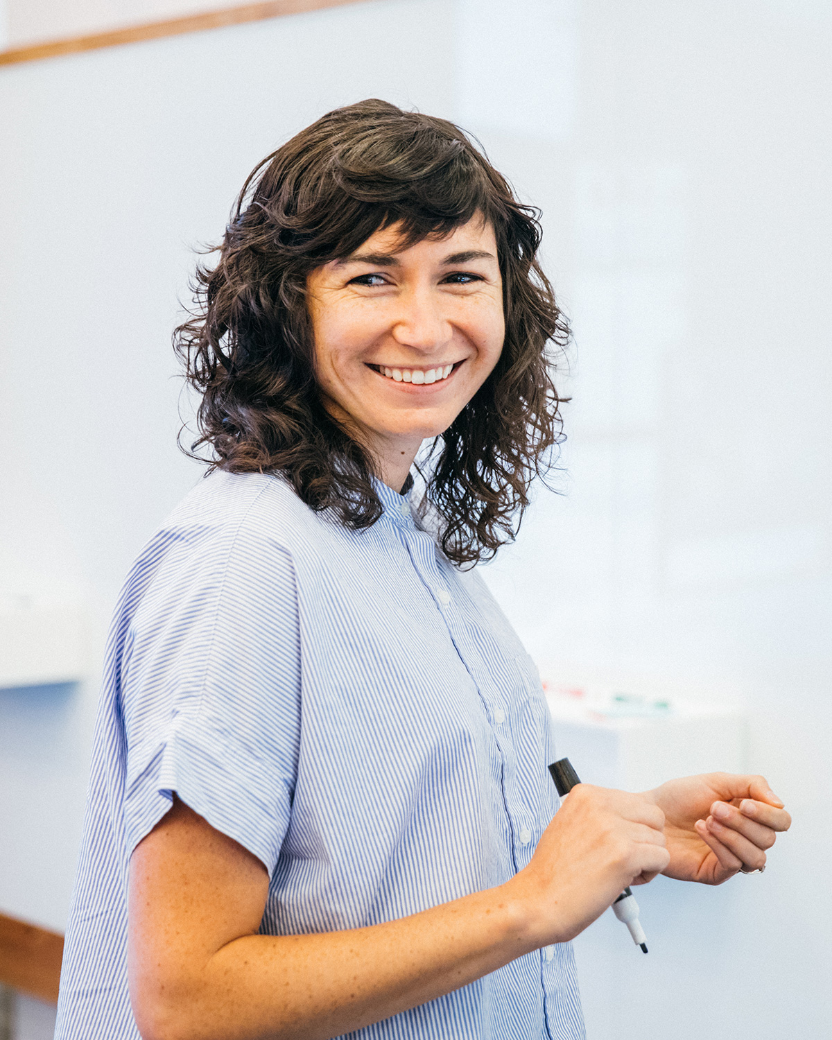 A woman smiling as she holds a whiteboard pen.