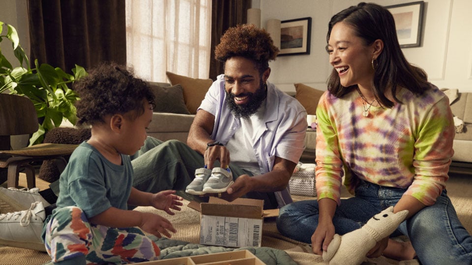 Family sitting on living room floor opening baby's shoes from shipping box. 