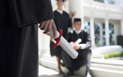 University student in graduation gown holding diploma, mid-section, focus on foreground