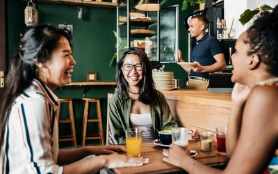 Three young friends sitting down in their favorite coffee shop, laughing and catching up with each other.