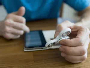 man holding fidget spinner while using smartphone