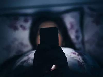 Woman texting and reading on smartphone in bed in midnight