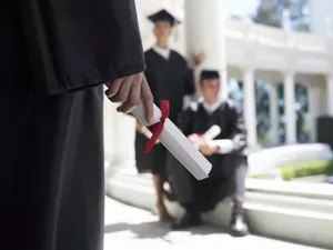 University student in graduation gown holding diploma, mid-section, focus on foreground