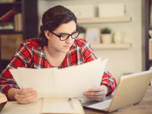 young woman looking at papers next to laptop