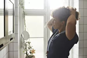 woman tying her hair in bathroom mirror