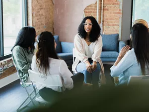 The young adult woman nervously speaks out during a meeting with her co-workers.