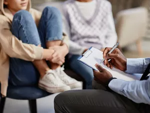 Close up of African-American psychologist taking notes on clipboard in therapy session for children