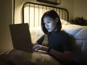 Woman working on her laptop in her bedroom at night