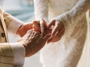 Bride putting ring on groom's finger. Rings exchange. Happy couple celebrating wedding outdoors in summer.