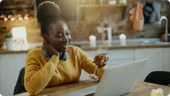 Woman holding a glass of wine while on her laptop.