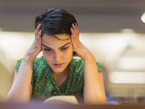 Female student with hands on her head studying in library