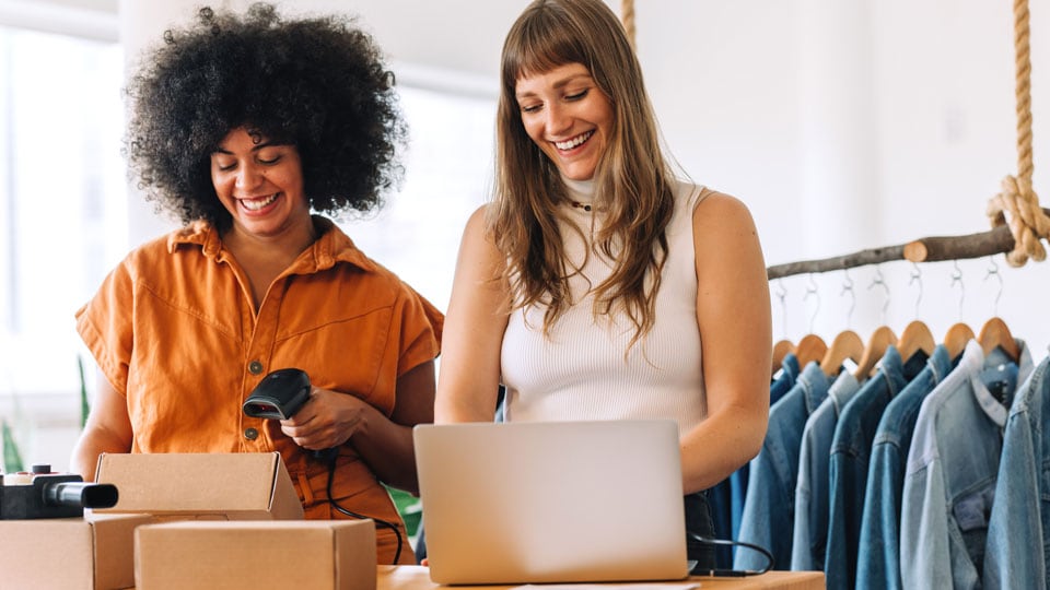 Two women working in clothing store smiling.