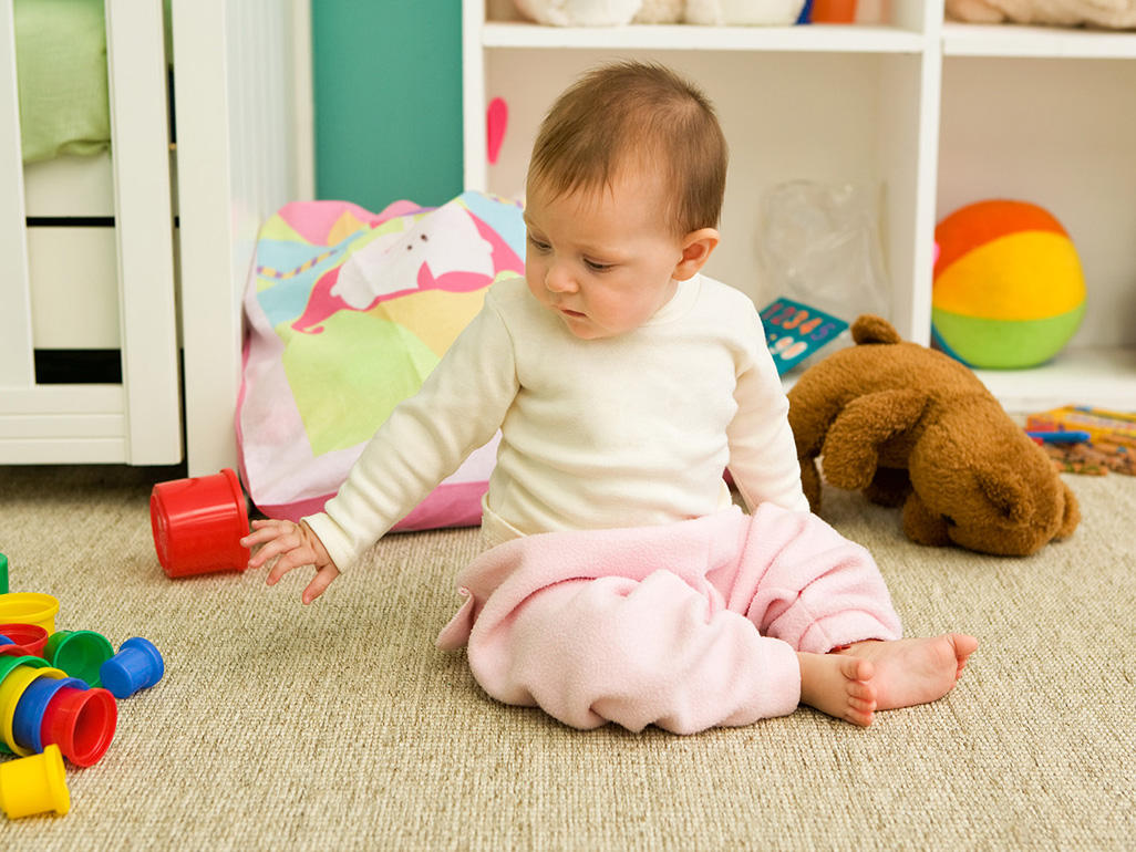 Baby girl in her nursery sitting on the floor playing with toys