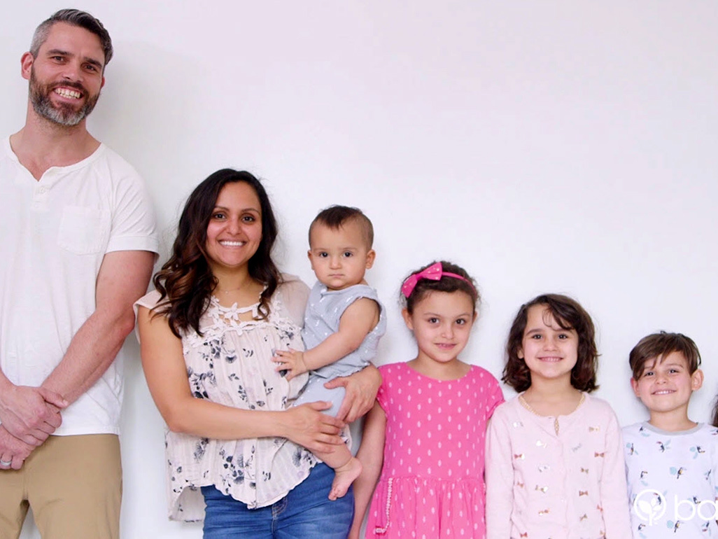 Family lined up against a white wall, standiing in height order and all smiling at the camera