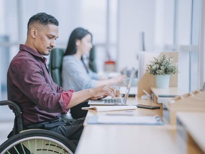 Latino man in wheelchair typing on laptop at office