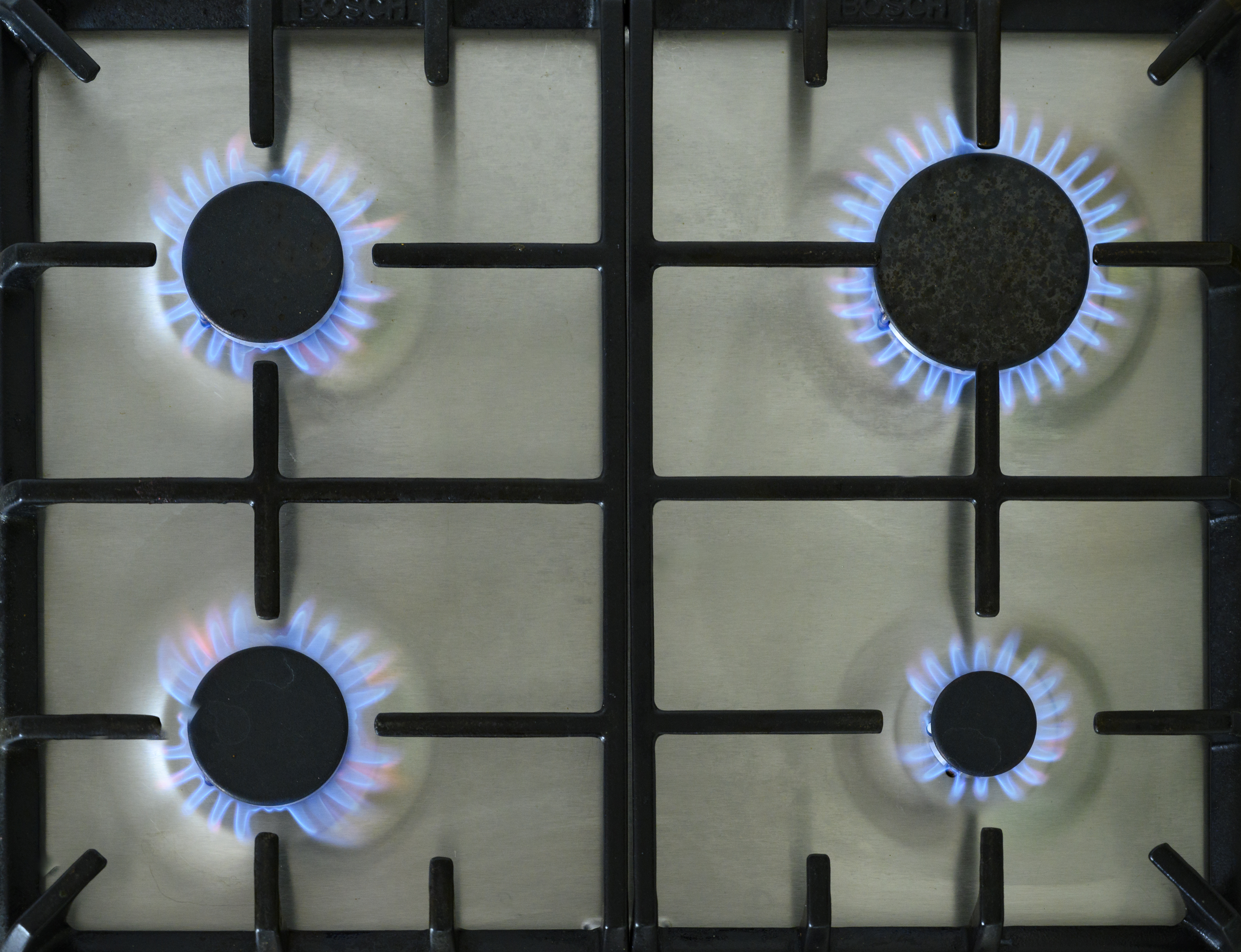 Four lit gas burners on a stove, seen from above.