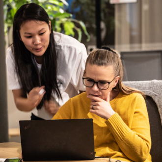 Three women are looking at a computer screen and conversing.