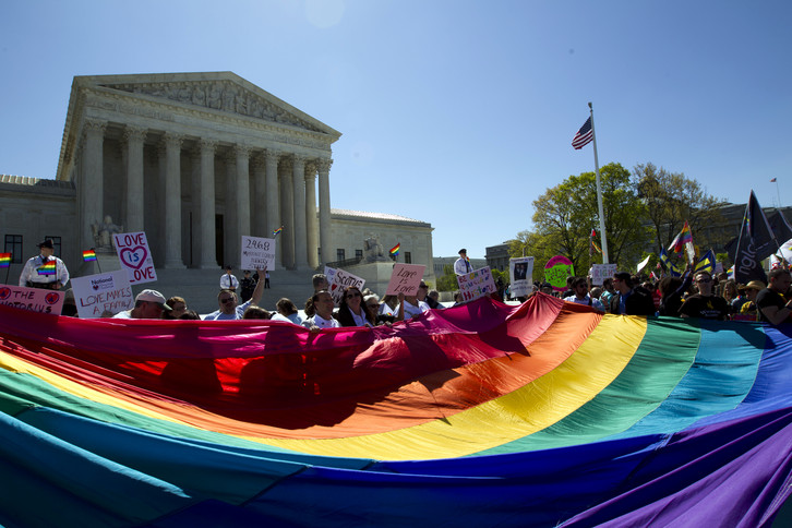 Demonstrators stand in front of a rainbow flag of the Supreme Court.