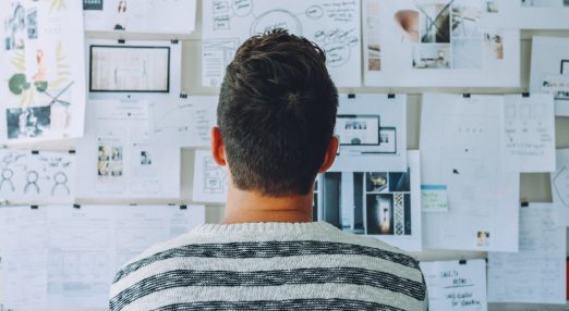 Man wearing black and white shirt looking at white printer papers on the wall