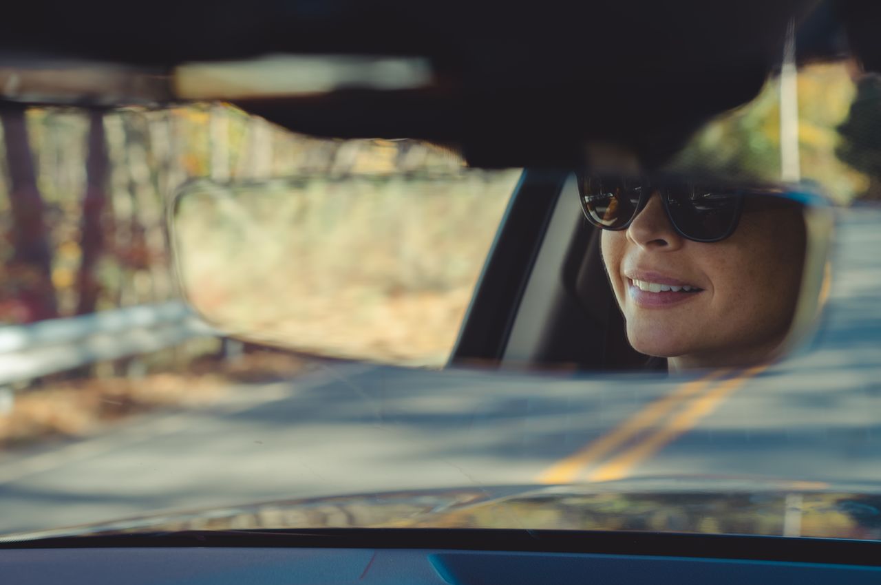 A smiling face in the rear view mirror of the car.