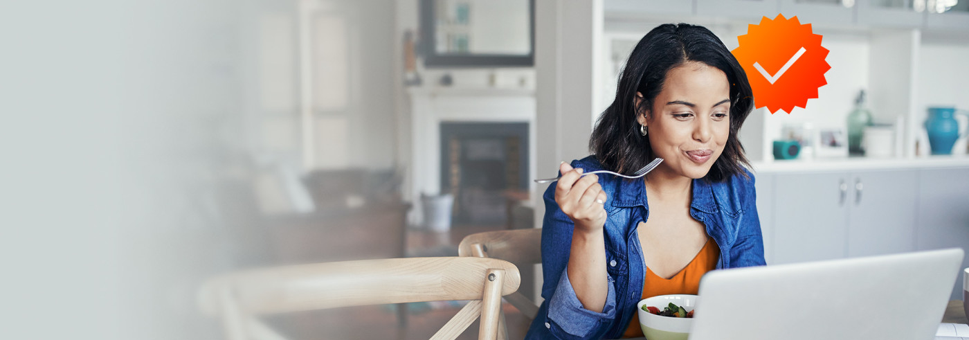 Woman on laptop eating bowl of fruit.