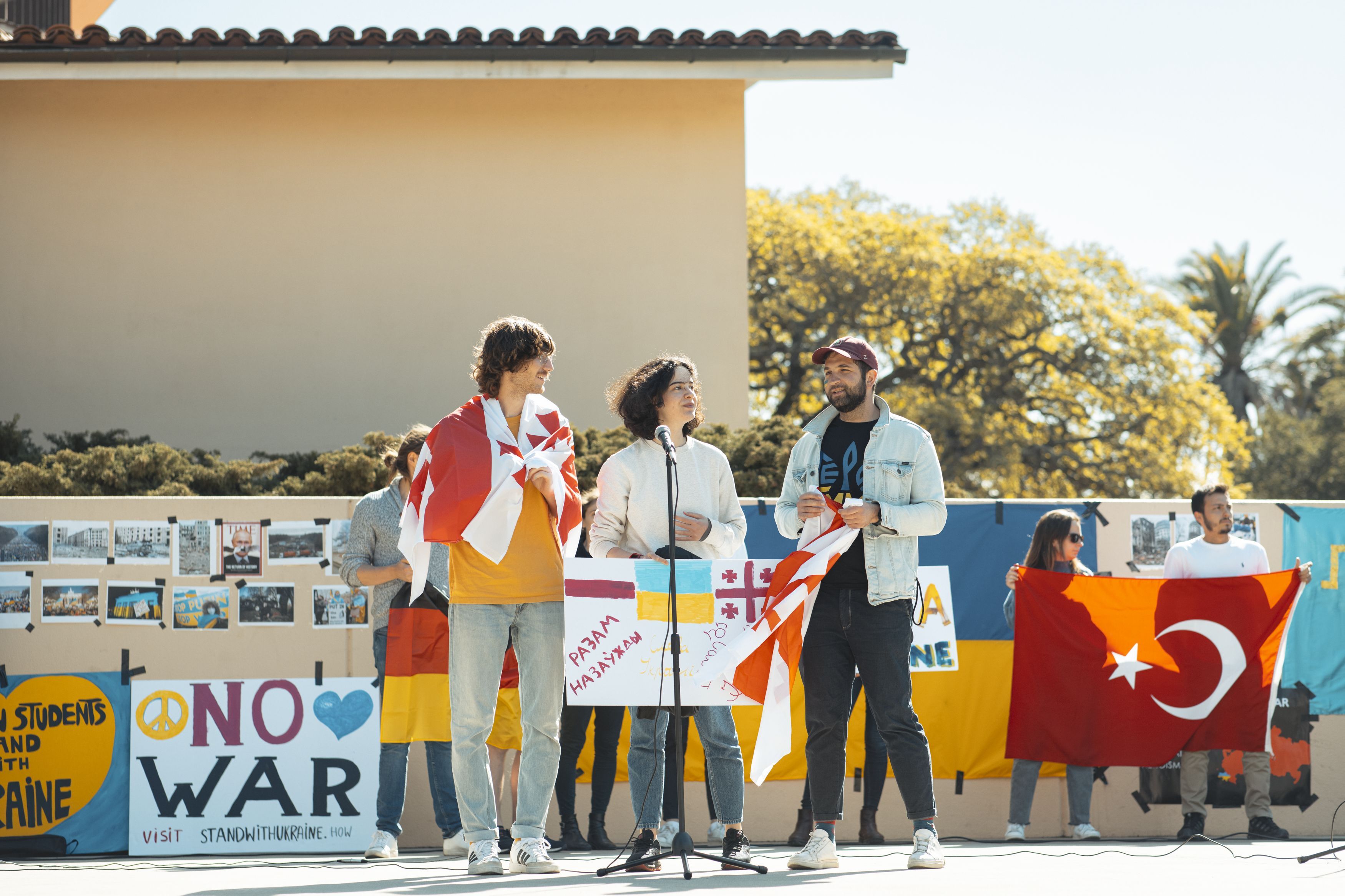 Members of the community step up to the mic while holding their countries' flags to stand in solidarity with Ukraine