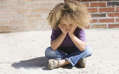 Sad, mixed race boy sitting on sidewalk