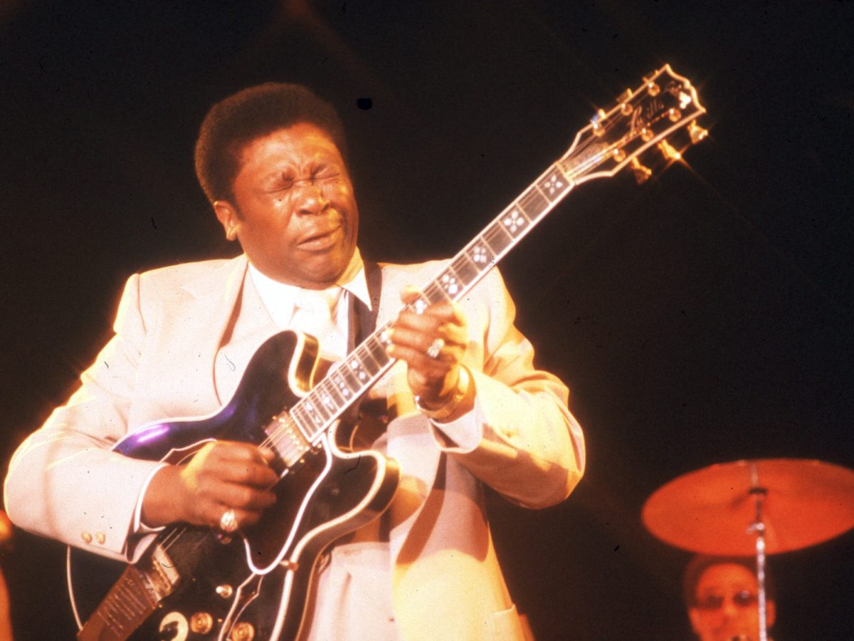 Man in a suit playing guitar onstage, his face overcome with emotion