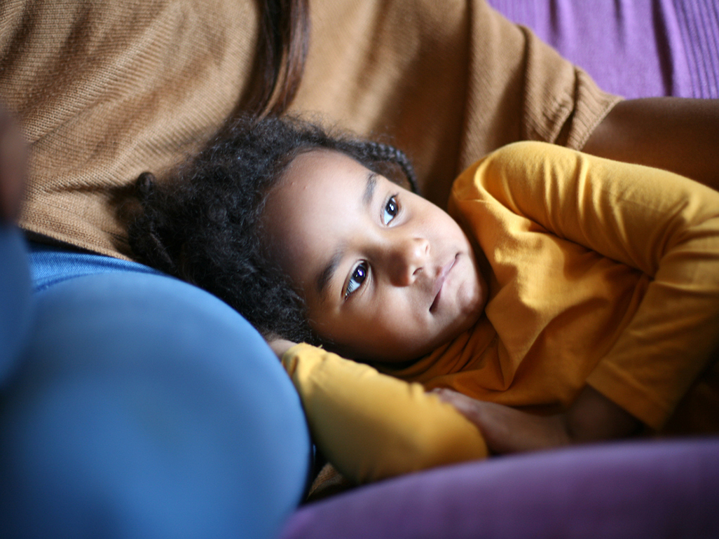 child resting on a mother’s leg who is sitting on a couch