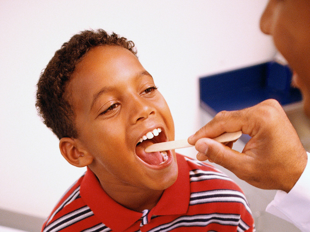 doctor examining boy's throat with a wooden tongue depressor