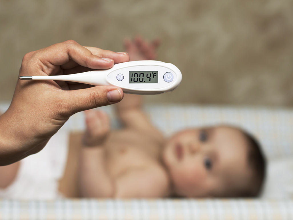 woman's hand with thermometer in front of a lying down baby