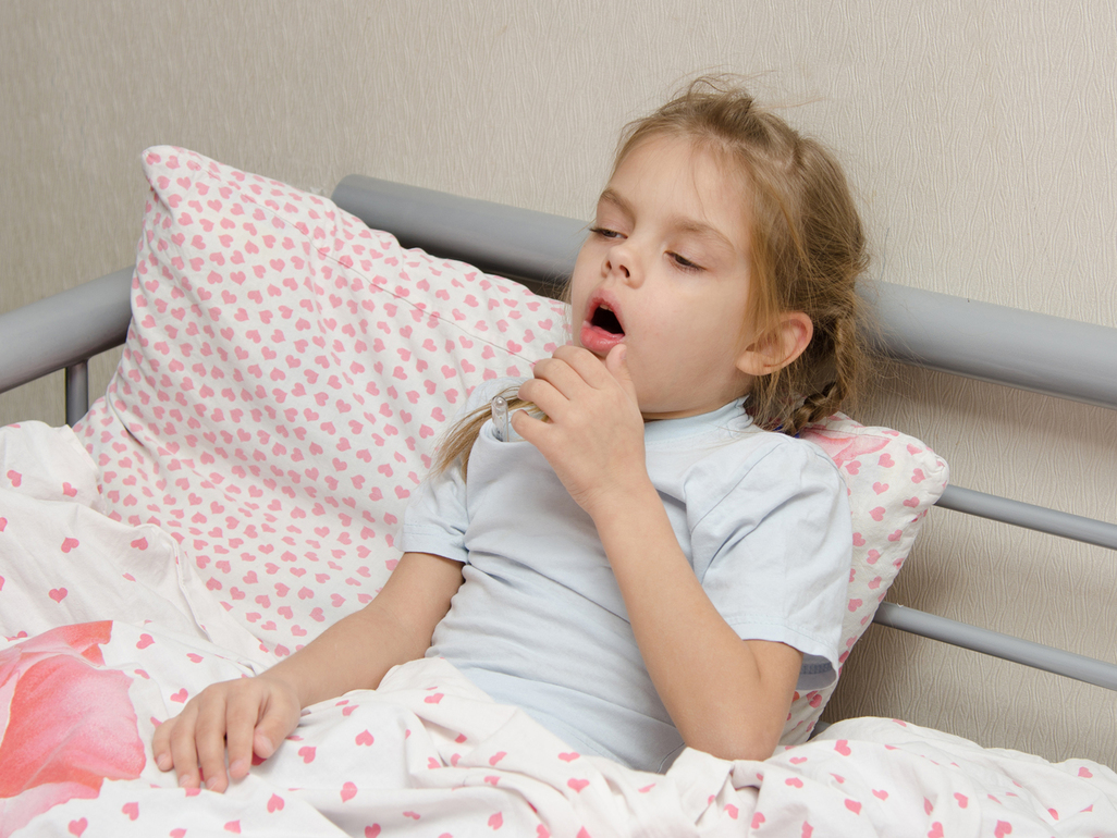 young girl coughing while sitting in bed