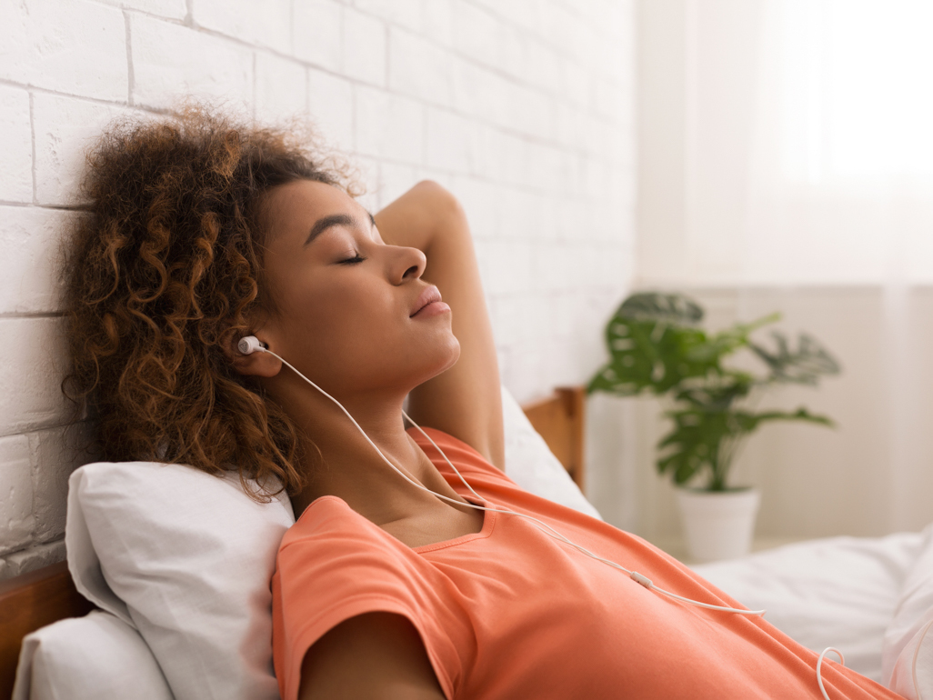 Black woman relaxing in bed with earbuds in