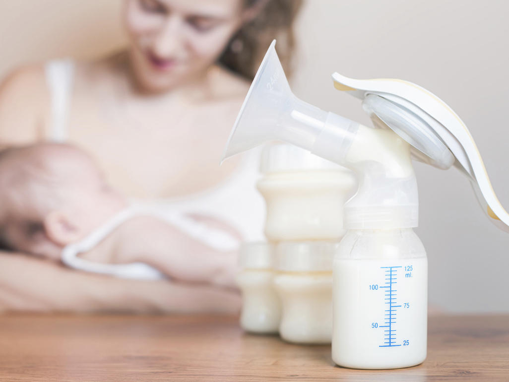 Breastmilk pump in the foreground while a mum feeds her baby in the background