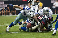 Photograph of defensive players tackling an offensive player who has just lost control of the football