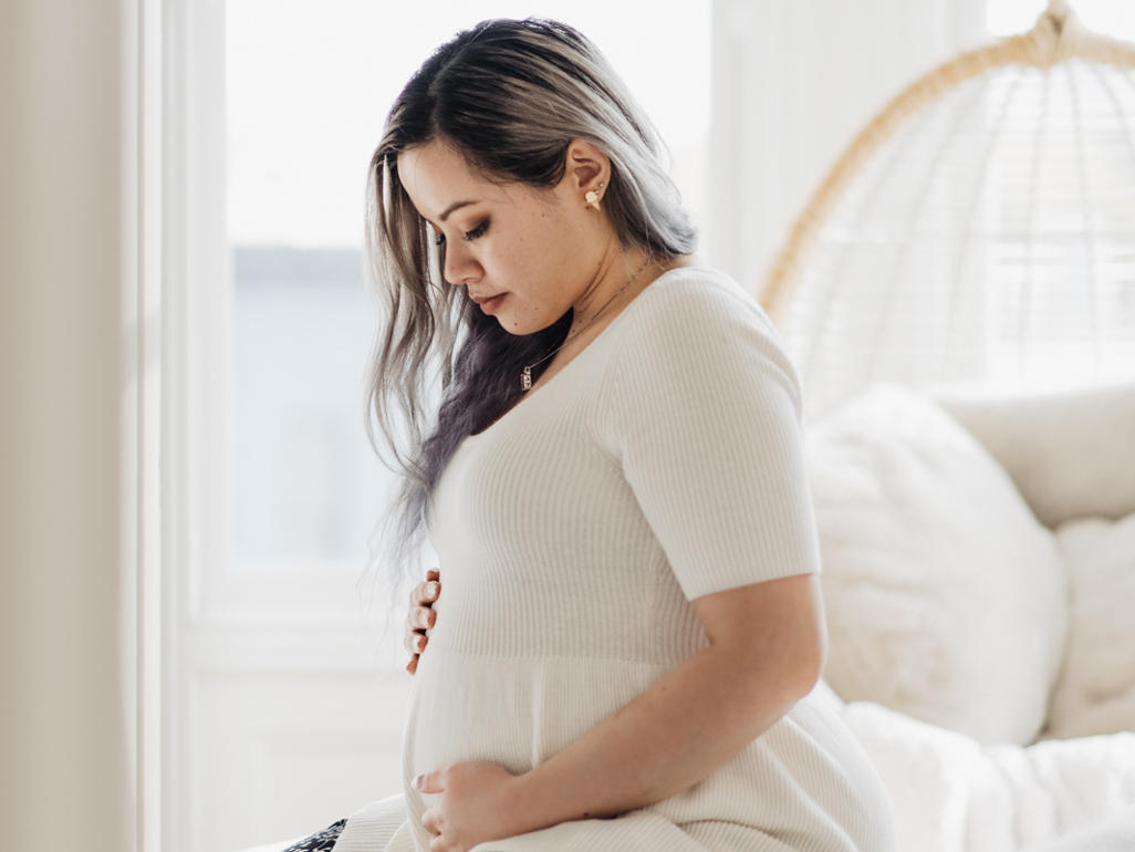 Pregnant woman sitting on her bed, looking down at her bump